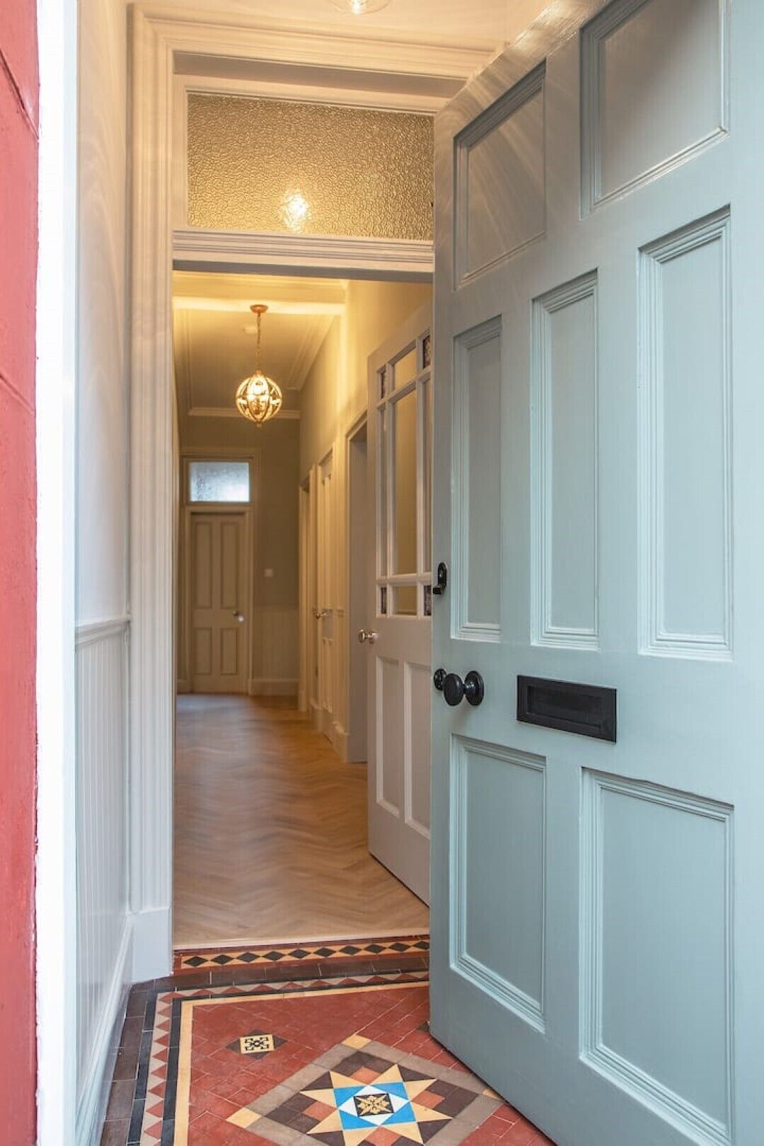 A hallway with a light blue door, a patterned rug, and a chandelier.