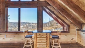A wooden interior with a table and chairs, large windows offering a view of a landscape.