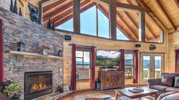A spacious living room with a stone fireplace, leather sofas, and a large window overlooking a scenic landscape.