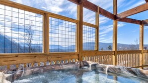 A hot tub with a wooden deck and large windows overlooking a mountainous landscape.