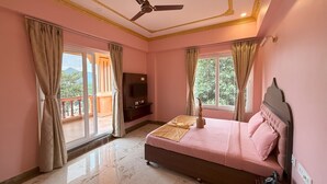 A bedroom with a bed, a ceiling fan, a TV, and a balcony with curtains.