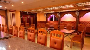 A dining area with marble tables and wooden chairs, a stage with curtains, and a cushioned seating area.