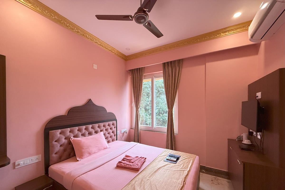 Een slaapkamer met een bed, een plafondventilator, een raam met gordijnen en een aan de muur bevestigde televisie.