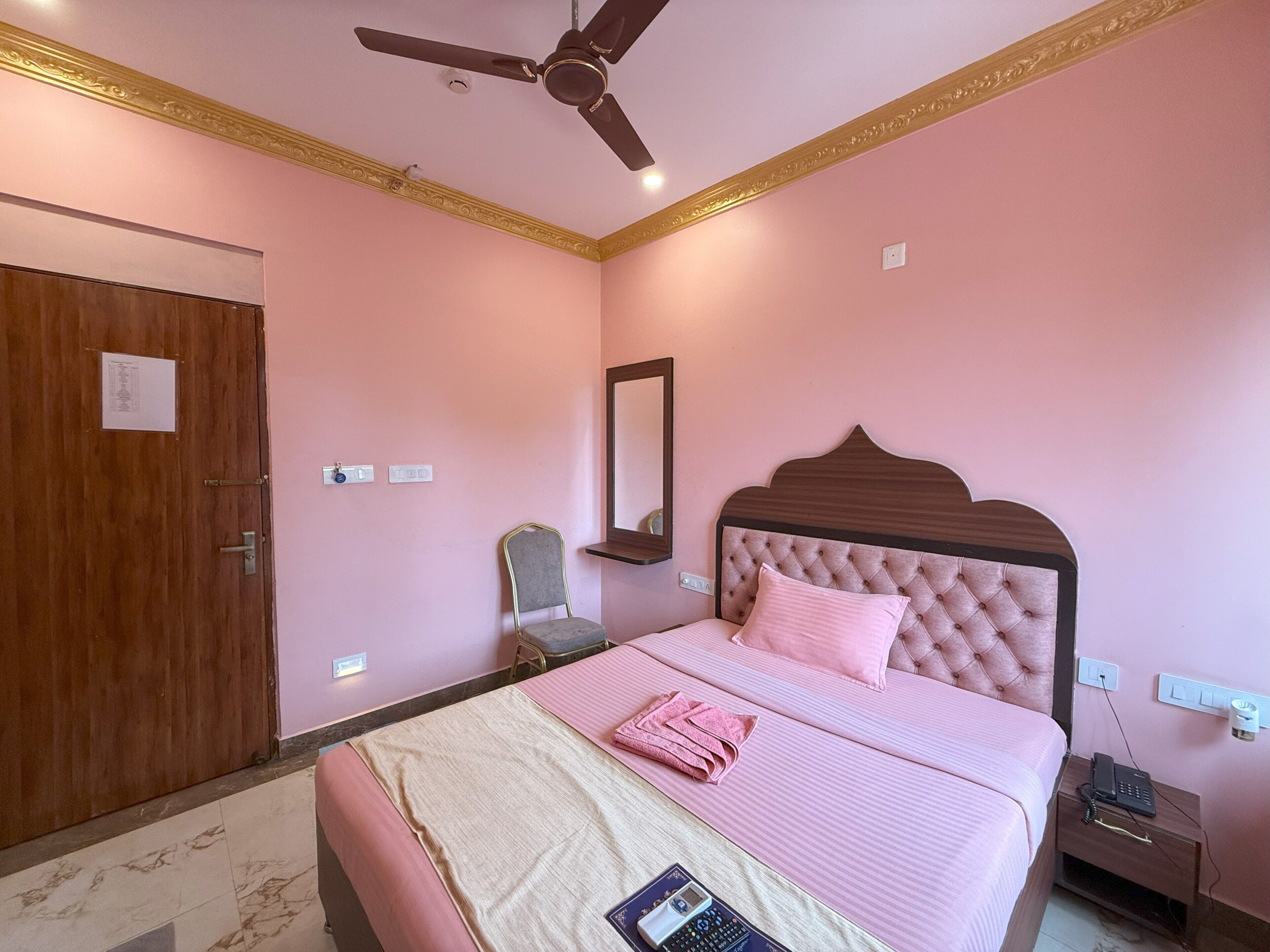 A bedroom with a bed, a ceiling fan, a chair, a nightstand, and a mirror.