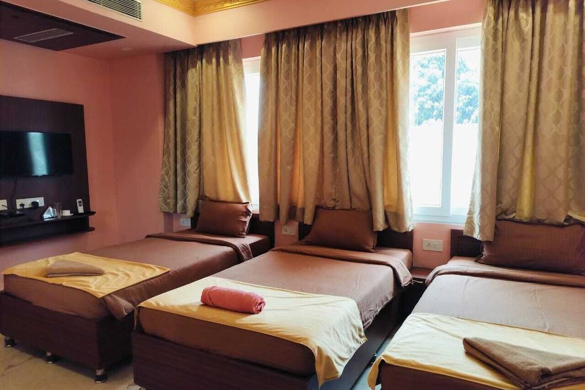 Een hotelkamer met vier bedden op rij, een flatscreen televisie aan de wand en grote ramen met gordijnen.