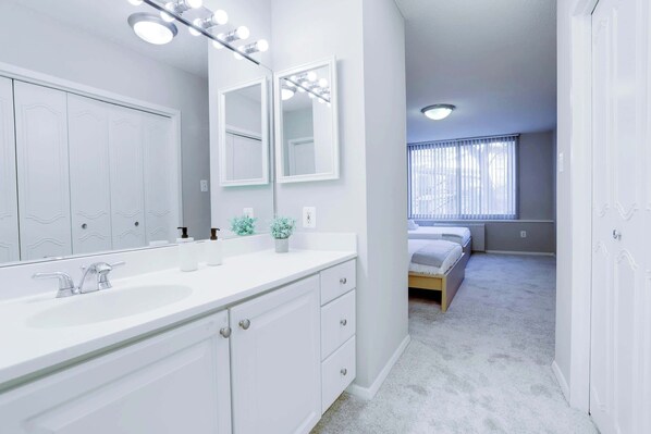 A modern bathroom with a large mirror, vanity, and a walk-in closet.