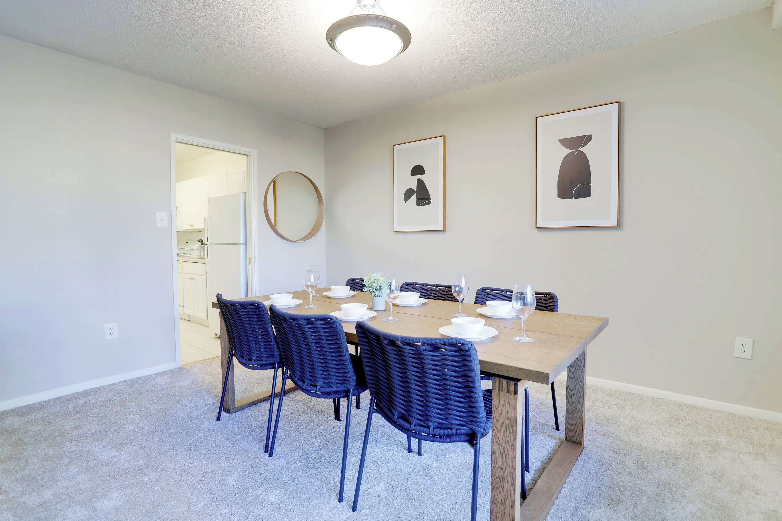 A dining area with a wooden table, six chairs, and framed artwork on the wall.