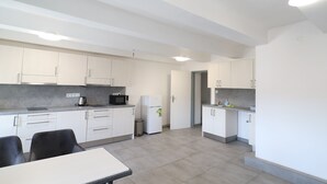 A modern kitchen with white cabinets, a microwave, a refrigerator, and a dining area with a table and chairs. - Apartmany a Hostel Plzen Rolnicke namesti (Plzen)