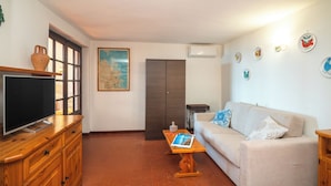 A living room with a television on a wooden cabinet, a sofa with patterned cushions, a coffee table with a book, and a map on the wall. - Trilo Triglia Cala Reale 229 (Golfo Aranci)