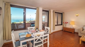 A dining area with a table set for two, a sofa, and a view of the sea. - Trilo Triglia Cala Reale 229 (Golfo Aranci)