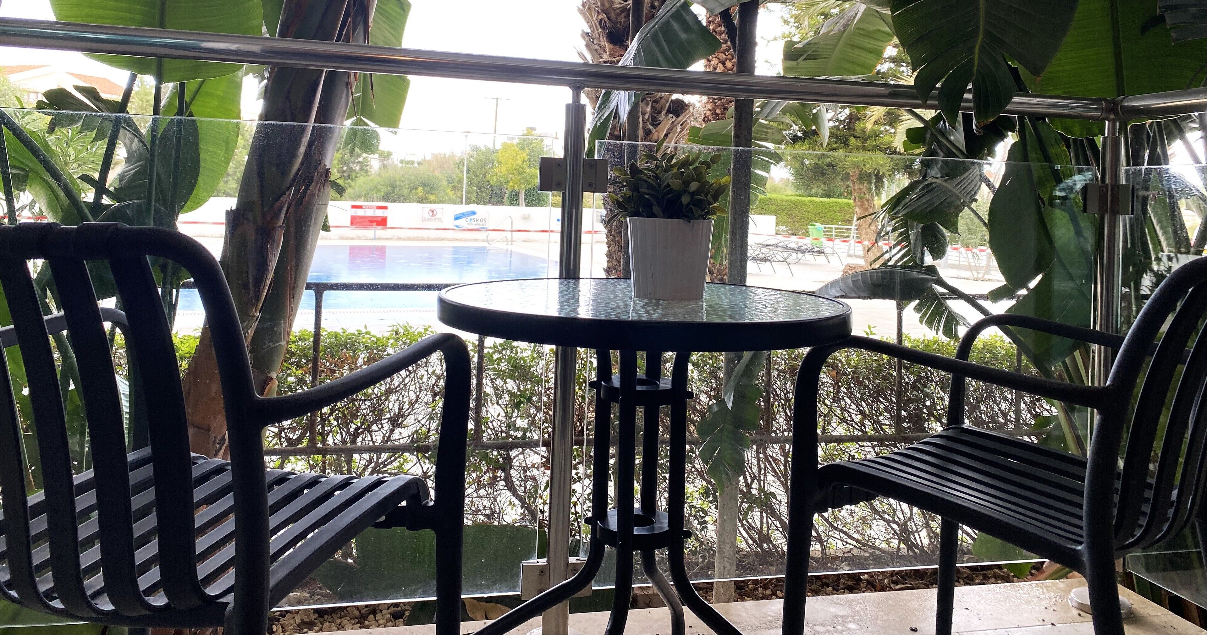 Ein Balkon mit zwei schwarzen Metallstühlen, einem kleinen runden Tisch und einem Blumentopf.