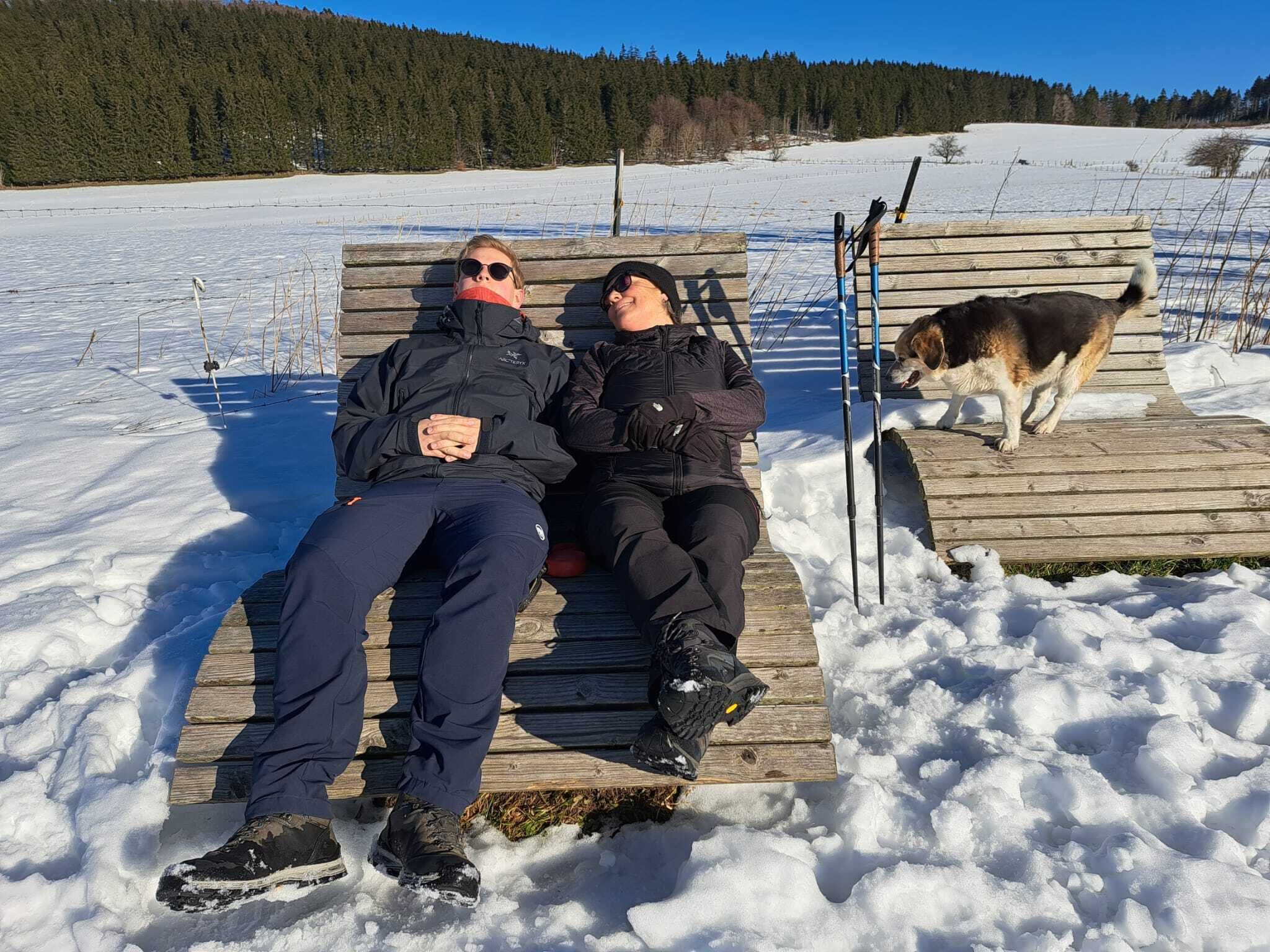 Two people sitting on a wooden bench in a snowy outdoor setting.