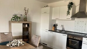 Une cuisine moderne avec des meubles blancs, une cuisinière en acier inoxydable et une table à manger en bois, assortie de chaises.
