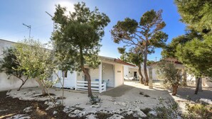 Ein Wohnhaus mit überdachter Terrasse, Garage und Garten mit Bäumen und Kieswegen.
