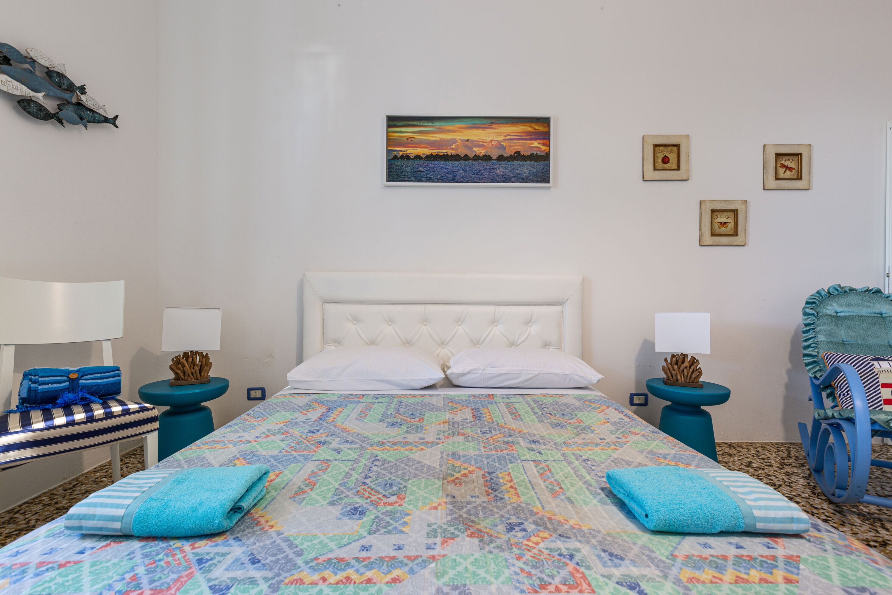 Une chambre à coucher avec un grand lit, deux tables de chevet, une chaise et un mur orné de tableaux.