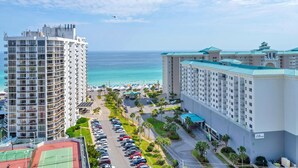 Un hotel de gran altura con vista al mar, un estacionamiento y una cancha de tenis.