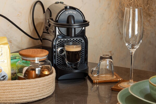 A coffee maker, a glass of water, and a woven basket with jars on a wooden table.