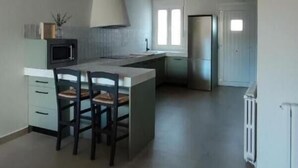 Une cuisine moderne dotée d’un îlot central, de poutres en bois au plafond et offrant une vue sur l’espace de vie.