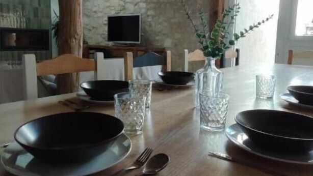 Une table à manger dressée avec des assiettes, des couverts et des verres, dans un intérieur rustique agrémenté de poutres apparentes et de murs en pierre.