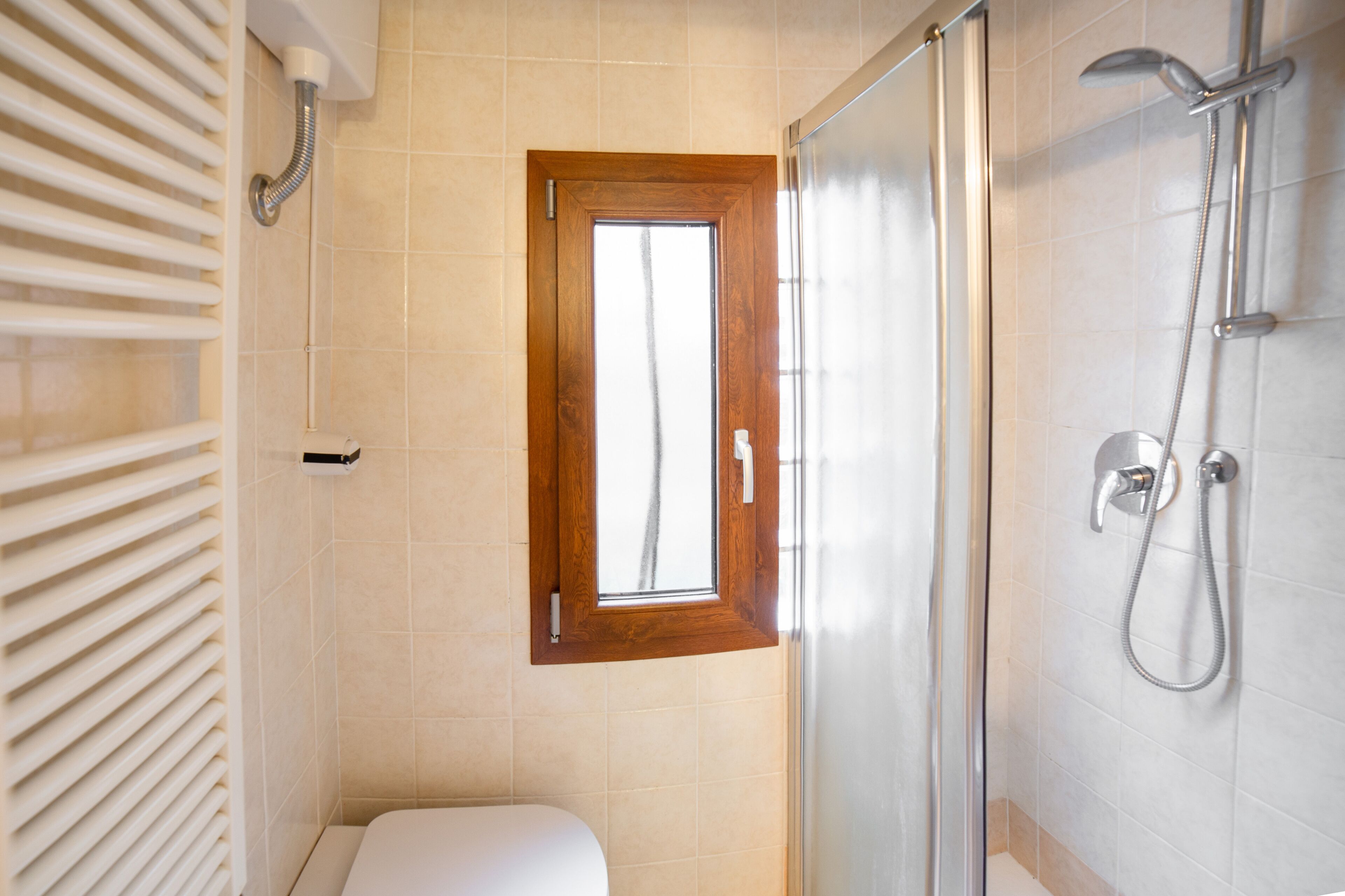 A bathroom with a shower, a toilet, and a window.