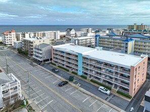 Ein mehrstöckiges Hotel mit Parkplatz davor, Blick auf den Strand und im Hintergrund eine Mischung aus Wohn- und Geschäftsgebäuden.