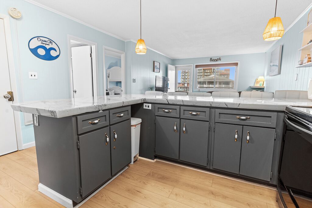 A kitchen with dark grey cabinets, a white countertop, and a view of the beach through the window.