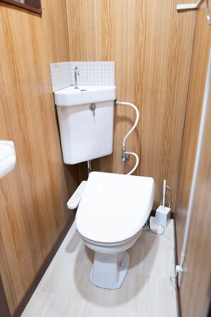 Une petite salle de bain aux dimensions réduites, avec des toilettes blanches, un lavabo blanc doté d’un pare-éclaboussures carrelé et un mur en bois.