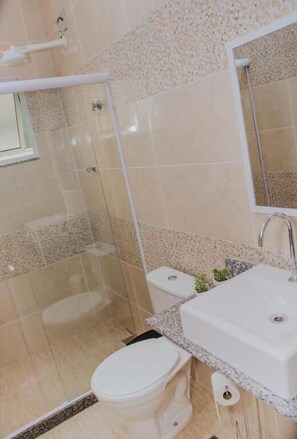 A bathroom with a glass-enclosed shower, a toilet, and a sink with a mirror. - Pousada La Brisa (Itaguai)