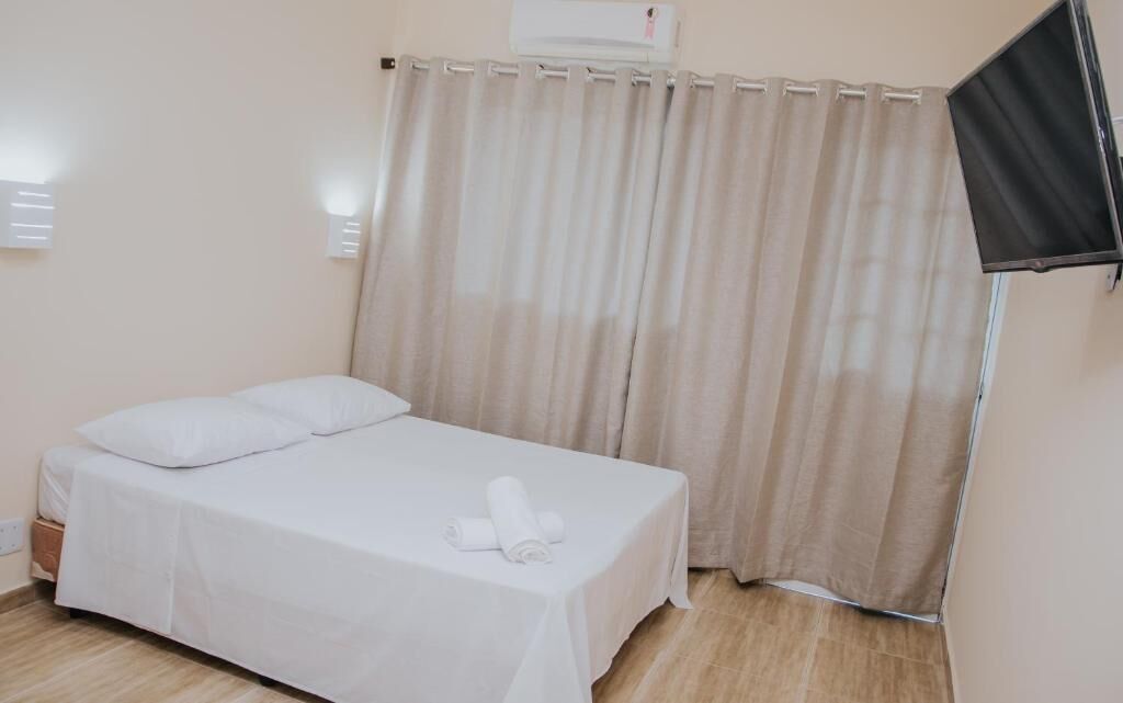 Een enkel bed met witte lakens, een opgerolde handdoek en een flatscreen televisie aan de muur.