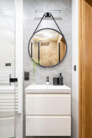 A modern bathroom with a white vanity, a round mirror, and a vase with flowers. - Apartamenty Harenda Zakopane (Zakopane)