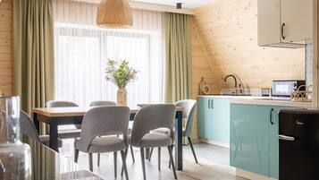 A modern kitchen with teal cabinets, a dining area with grey chairs, and a large window with sheer curtains.