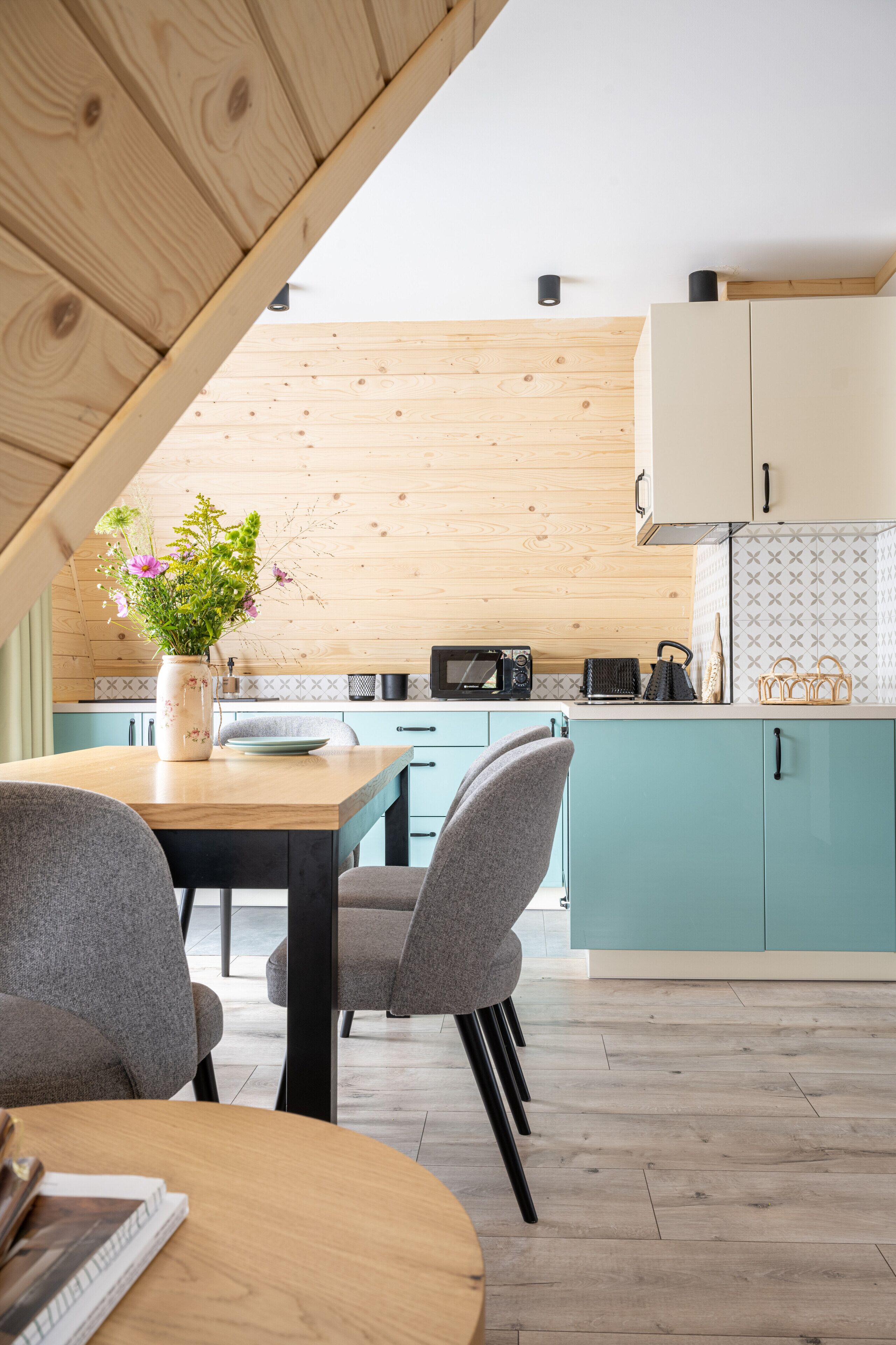 A modern kitchen with teal cabinets, a wooden ceiling, and a dining area with a table and chairs.