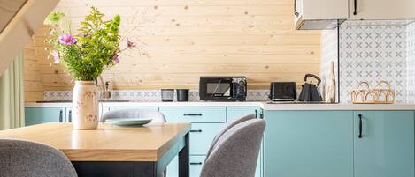 A modern kitchen with teal cabinets, a wooden ceiling, and a dining area with a table and chairs.