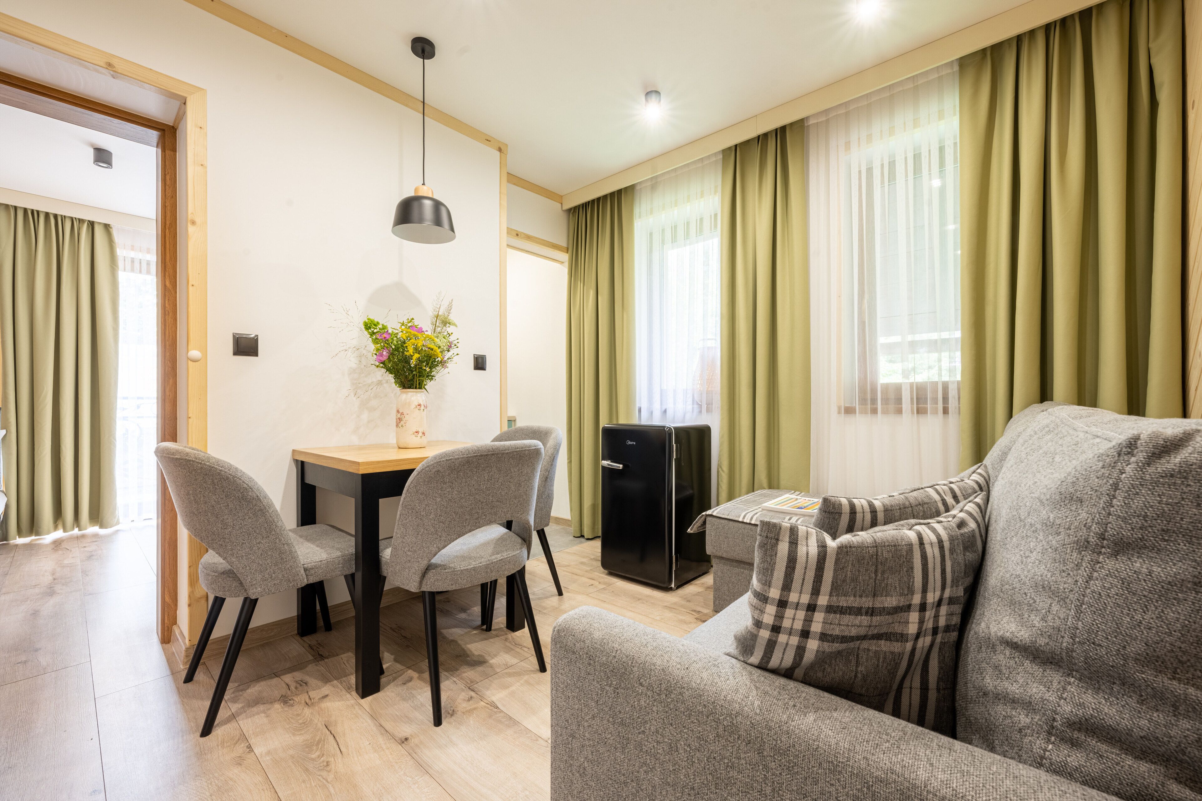 A modern living room with a sofa, dining table, chairs, and a small black refrigerator.