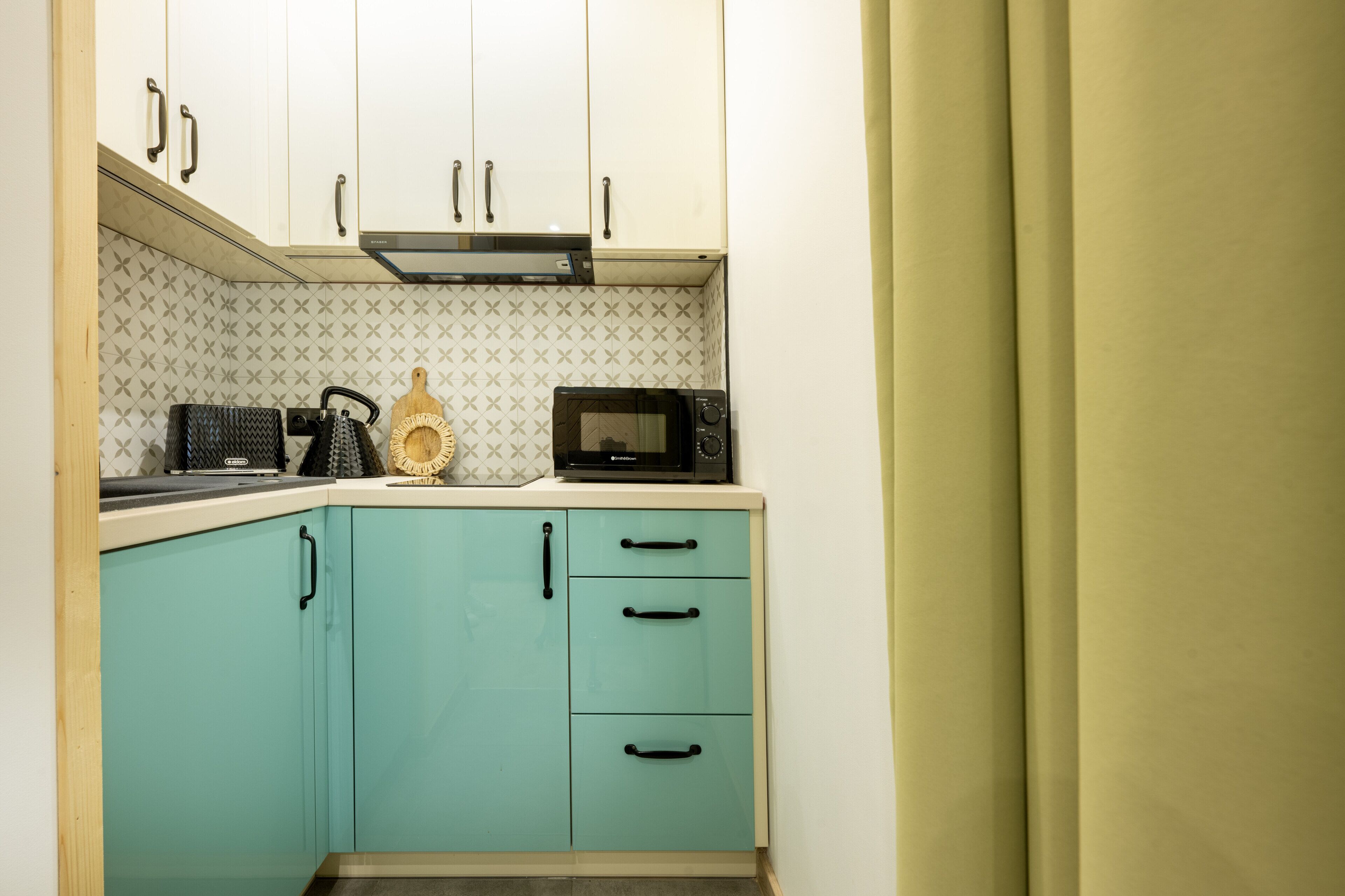 Cocina compacta con armarios verde azulado, microondas y cafetera.