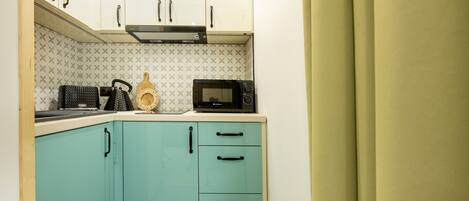 Cocina compacta con armarios verde azulado, microondas y cafetera.