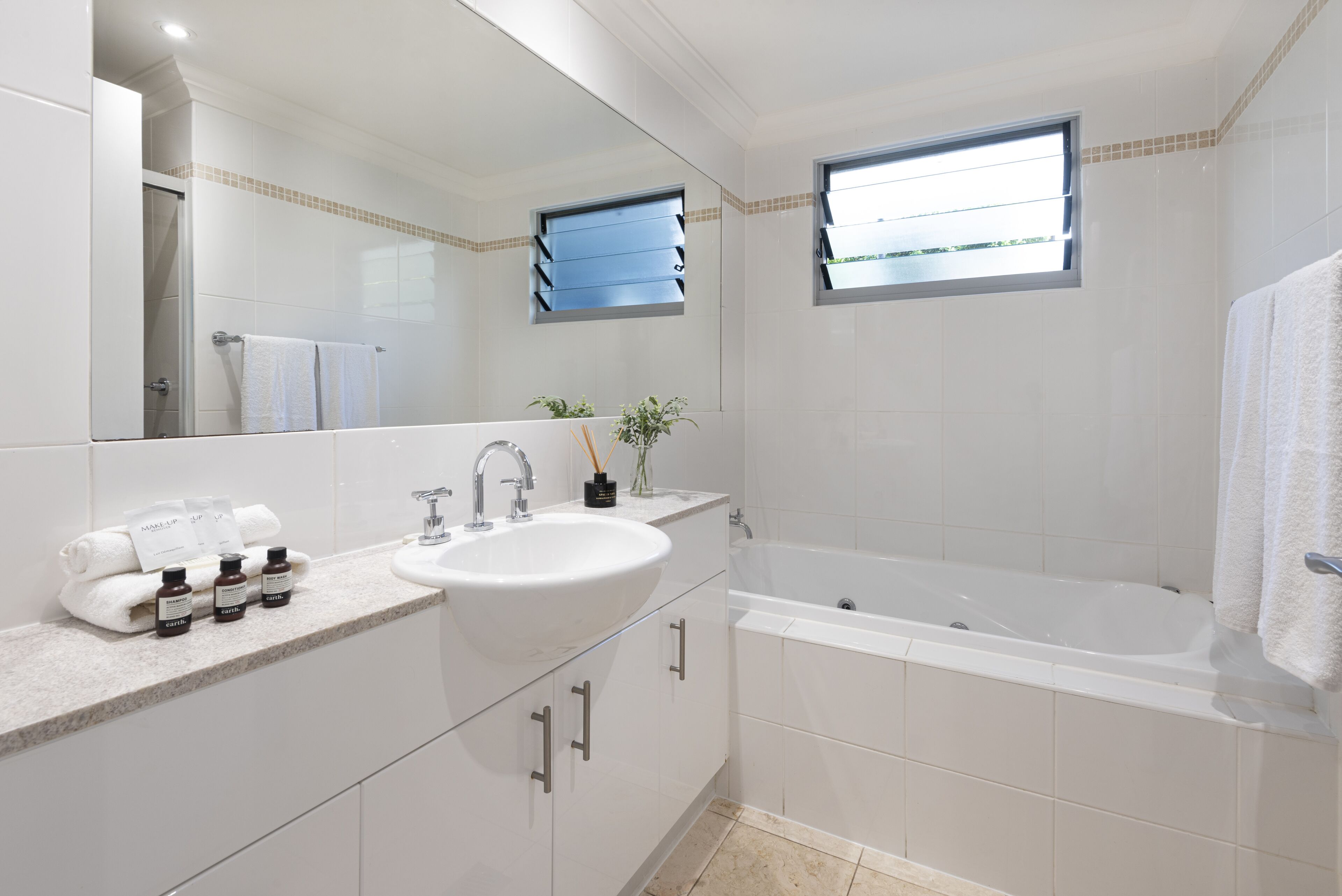 Une salle de bain moderne avec un grand lavabo, une baignoire et une fenêtre équipée de stores.