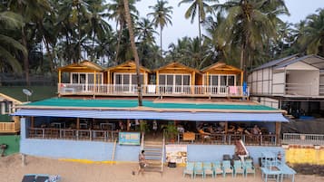 A beachfront resort with wooden cabins, a covered seating area, and a sign for Ayurvedic massage.
