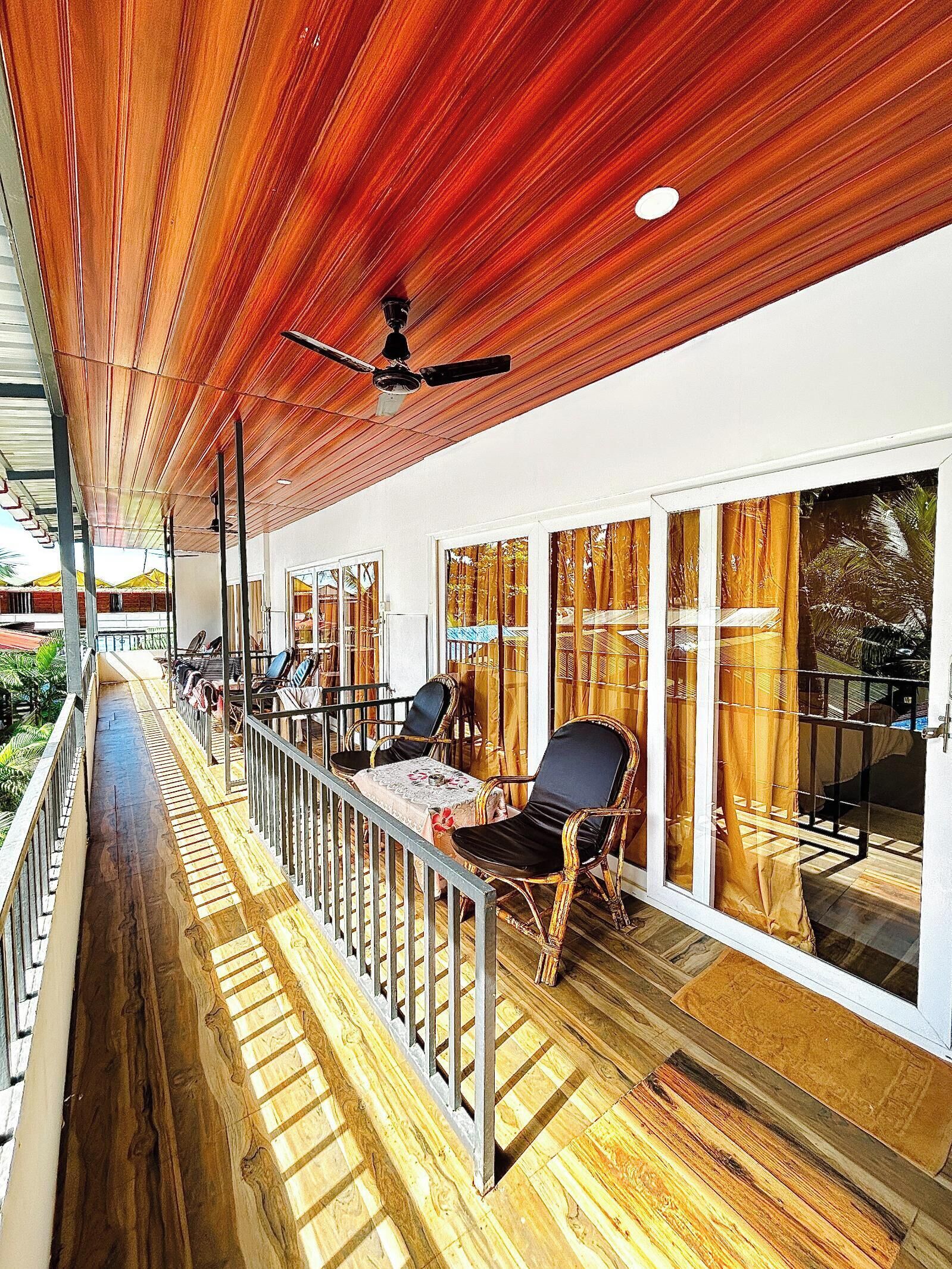 A covered outdoor area with wooden flooring, metal railings, and black chairs.