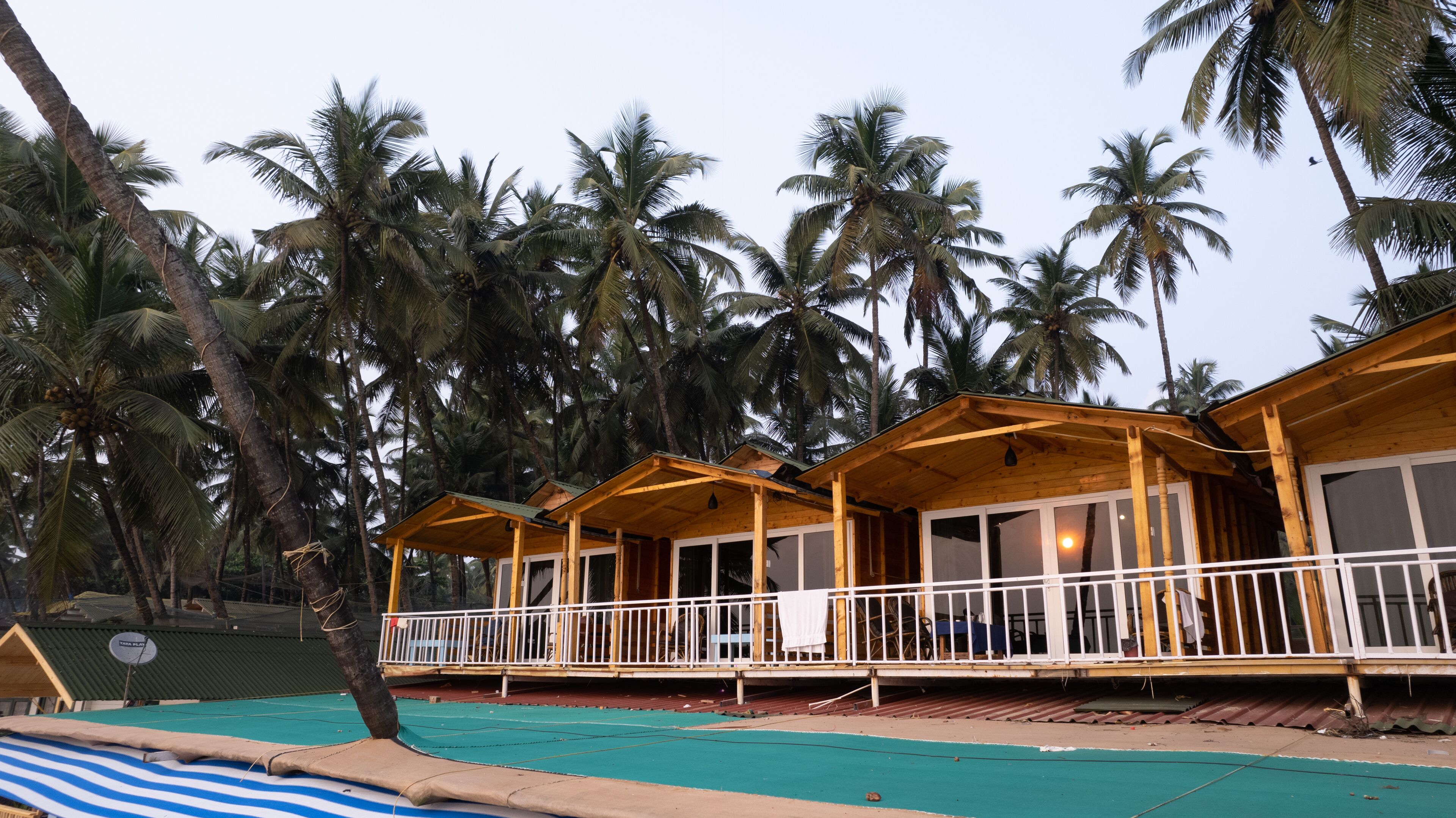 Una hilera de bungalows de madera con balcones, piscina y palmeras al fondo.