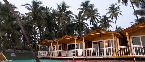 Una hilera de bungalows de madera con balcones, piscina y palmeras al fondo.