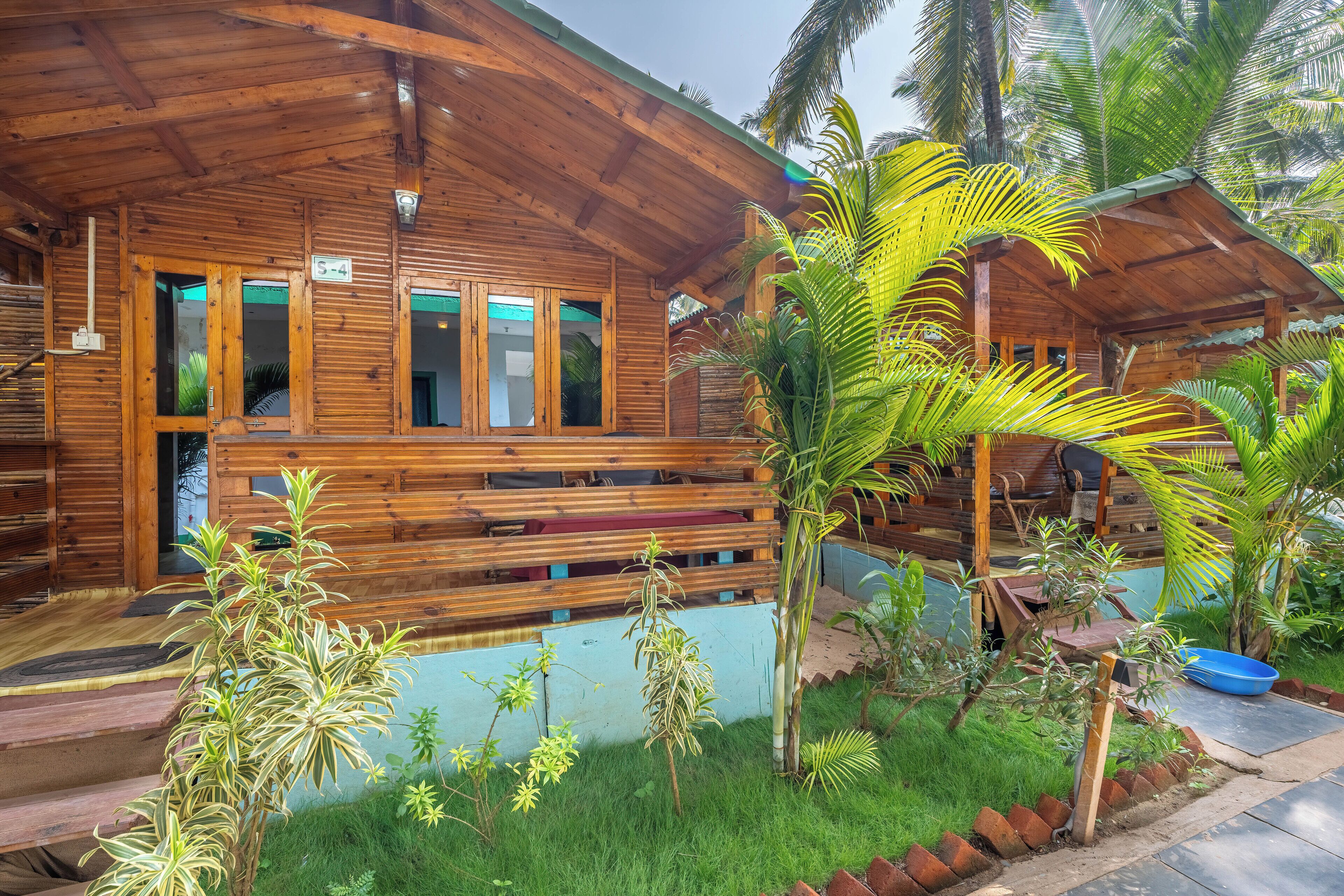 A wooden cabin with a porch, a small pool, and tropical plants.