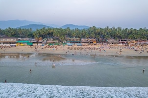 Une plage avec des gens, des palmiers et des bâtiments en arrière-plan.