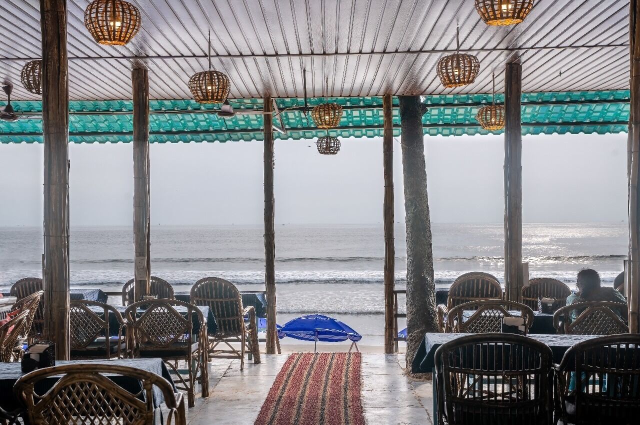 A covered outdoor seating area with tables and chairs, overlooking the ocean.