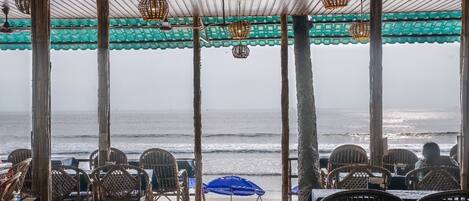 A covered outdoor seating area with tables and chairs, overlooking the ocean.