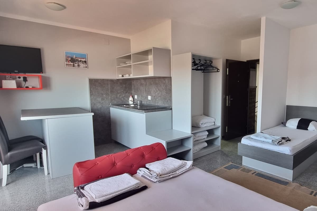 A modern hotel room with a bed, a desk, a chair, a TV, and a wardrobe.