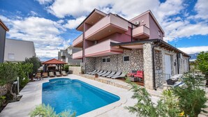 A modern building with a swimming pool, outdoor seating, and a stone facade. - Tiffany Novalja (Novalja)