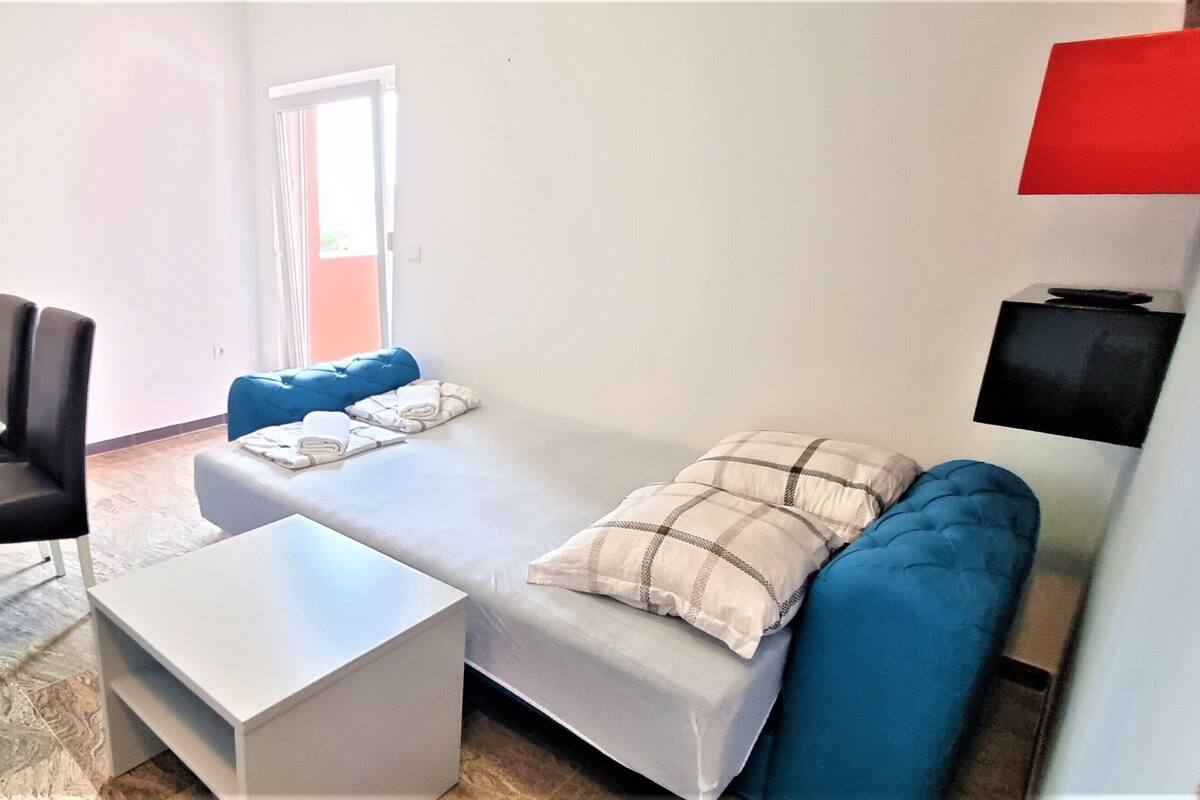 A compact living space with a sofa, a small table, a chair, and a TV mounted on the wall.