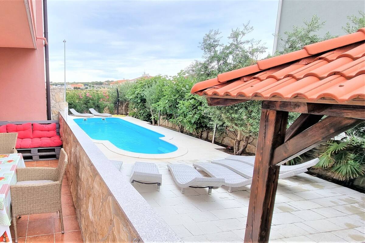 A poolside area with a table and chairs, a red sofa, and a view of the pool.