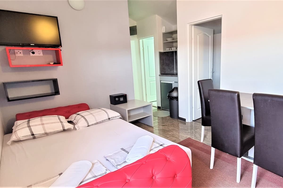A hotel room with a bed, a desk with chairs, a TV mounted on the wall, and a closet.